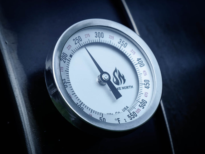 A Tel-Tru thermometer shown on the cook chamber door of an offset smoker, displaying a temperature reading of 250 degrees