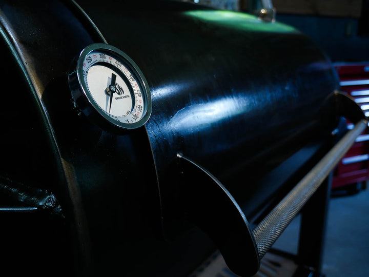 An offset smoker cook chamber door with a dark oiled finish, a stainless steel knurled door handle, and a Tel Tru thermometer with the 'Smoke North' logo printed in the design