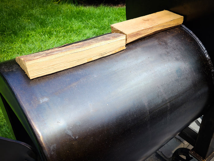 Two splits of wood shown preheating on top of the firebox of an offset smoker