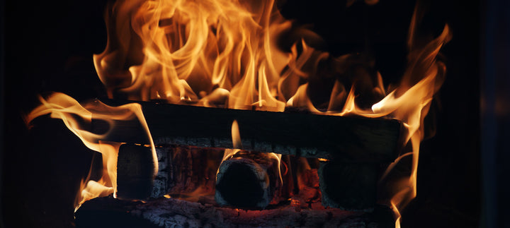 A large fire amongst stacked wood logs shown inside the firebox of an offset smoker